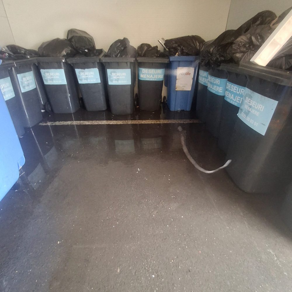 Cameră de colectare a deșeurilor după curățare, cu pardoseala spălată și pubelele aliniate